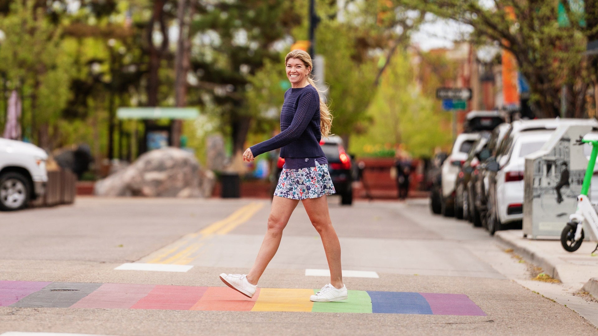 Woman enjoying the weekend walking across the street downtown in a blue sweater and floral skirt