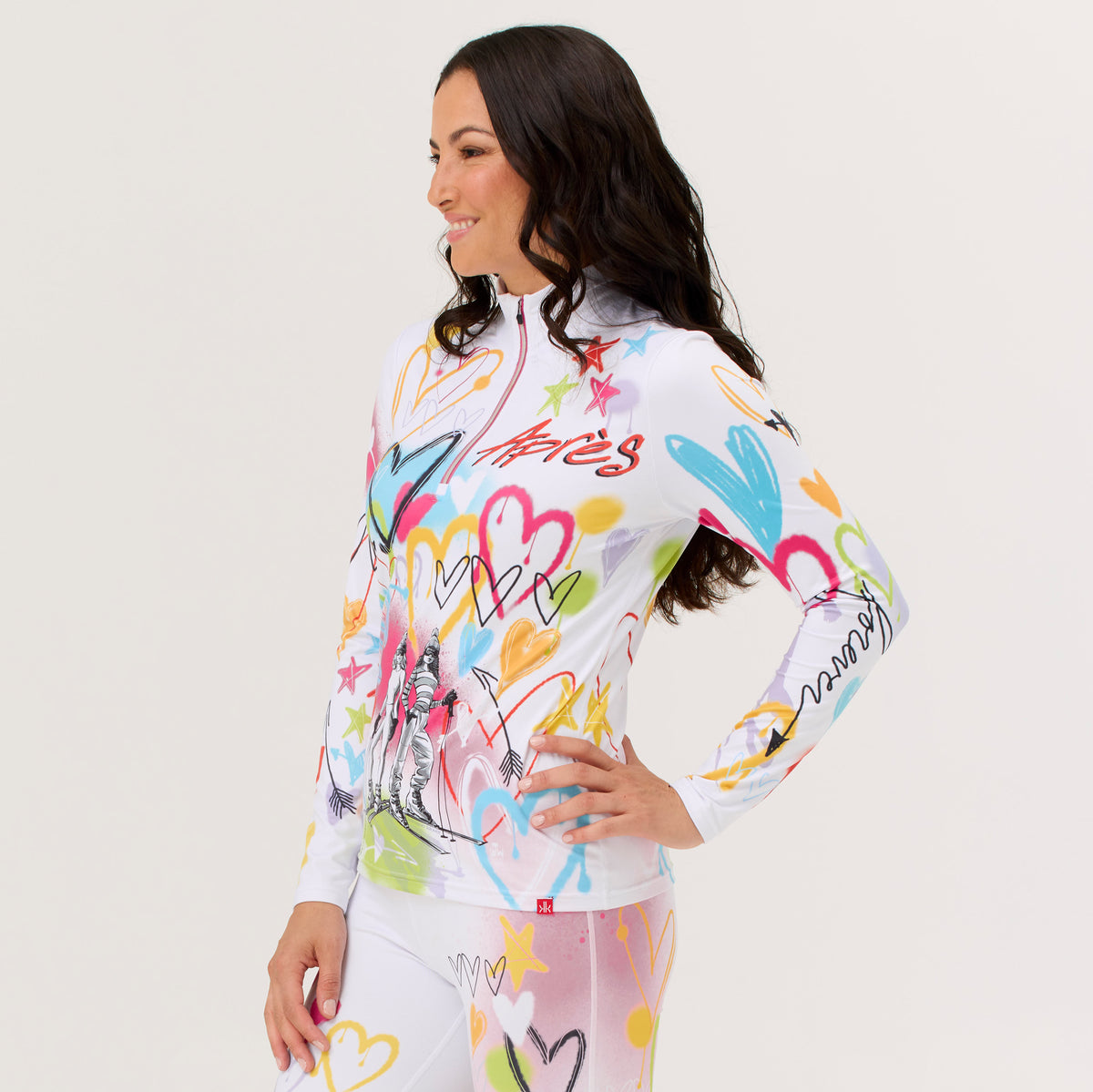A woman modeling a white long-sleeve base layer top and matching leggings with a colorful graffiti-style heart and star print, posed against a plain light background.