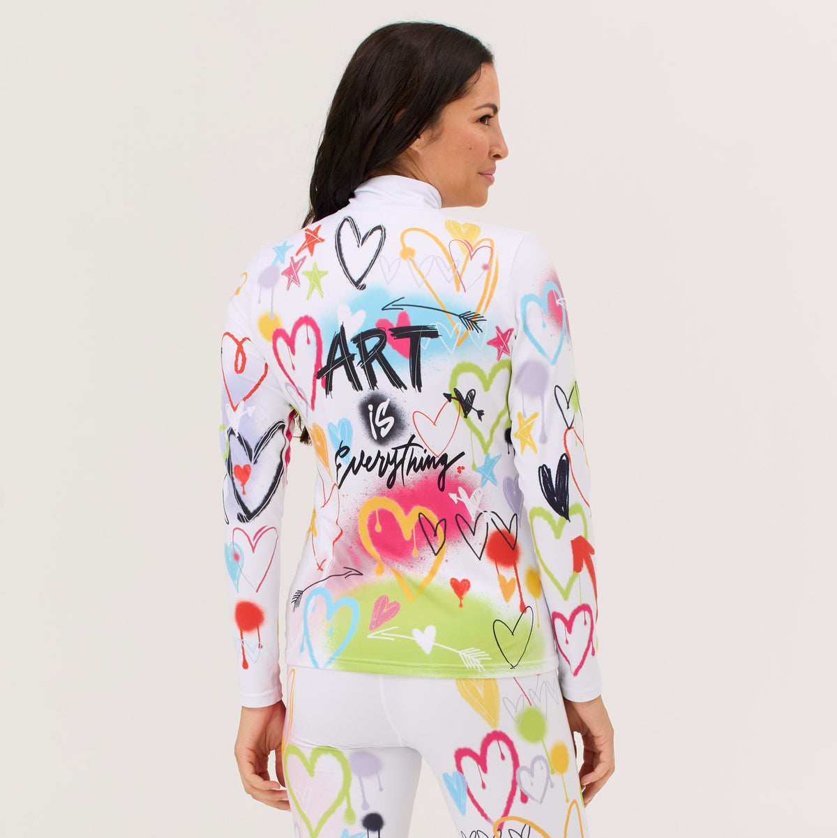 A woman shown from the back wearing a white long-sleeve athletic top and matching white leggings, both covered in colorful heart doodles and graffiti-style graphics. The back of the top features the text 'Art is Everything'.