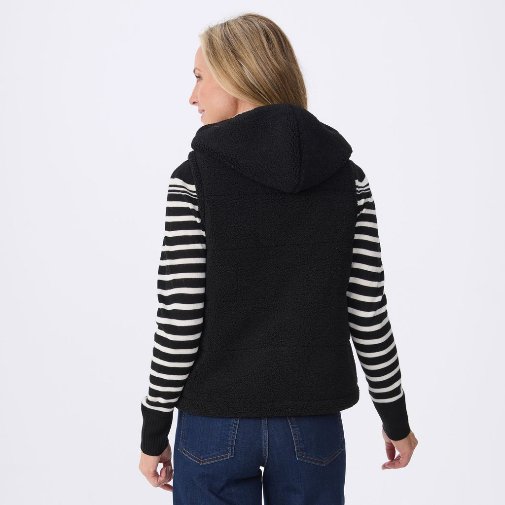 A woman shown from the back wearing a black fleece hooded vest over a black and white striped long-sleeve top, paired with blue jeans, against a plain white studio background.