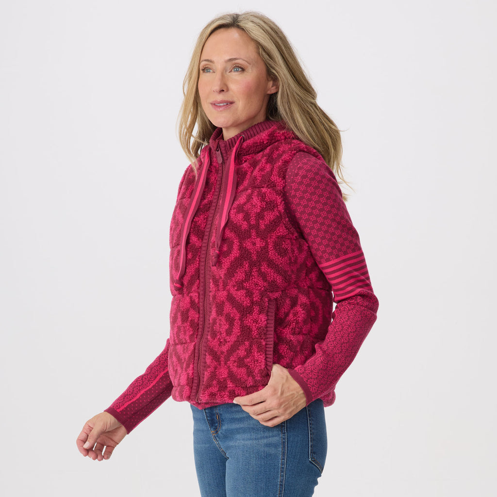 A woman modeling a pink and magenta patterned fleece zip-up hoodie vest, paired with blue jeans, against a light gray studio background.