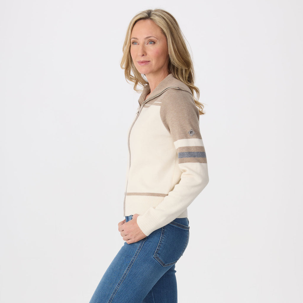 A woman modeling a cropped zip-up hoodie with cream and taupe color blocking and striped detailing on the sleeve, paired with blue jeans against a plain white studio background.