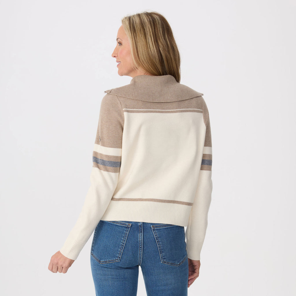 A woman shown from the back wearing a color-blocked knit sweater with a high ribbed collar, cream body, taupe shoulder and hem stripes, and blue jeans against a plain light gray studio background.