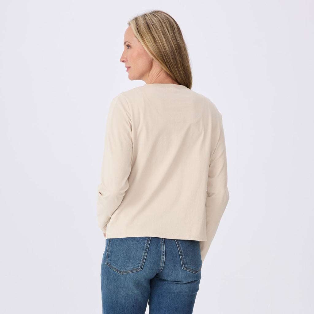 A woman shown from the back wearing a light beige long-sleeve top and blue jeans against a plain white studio background.