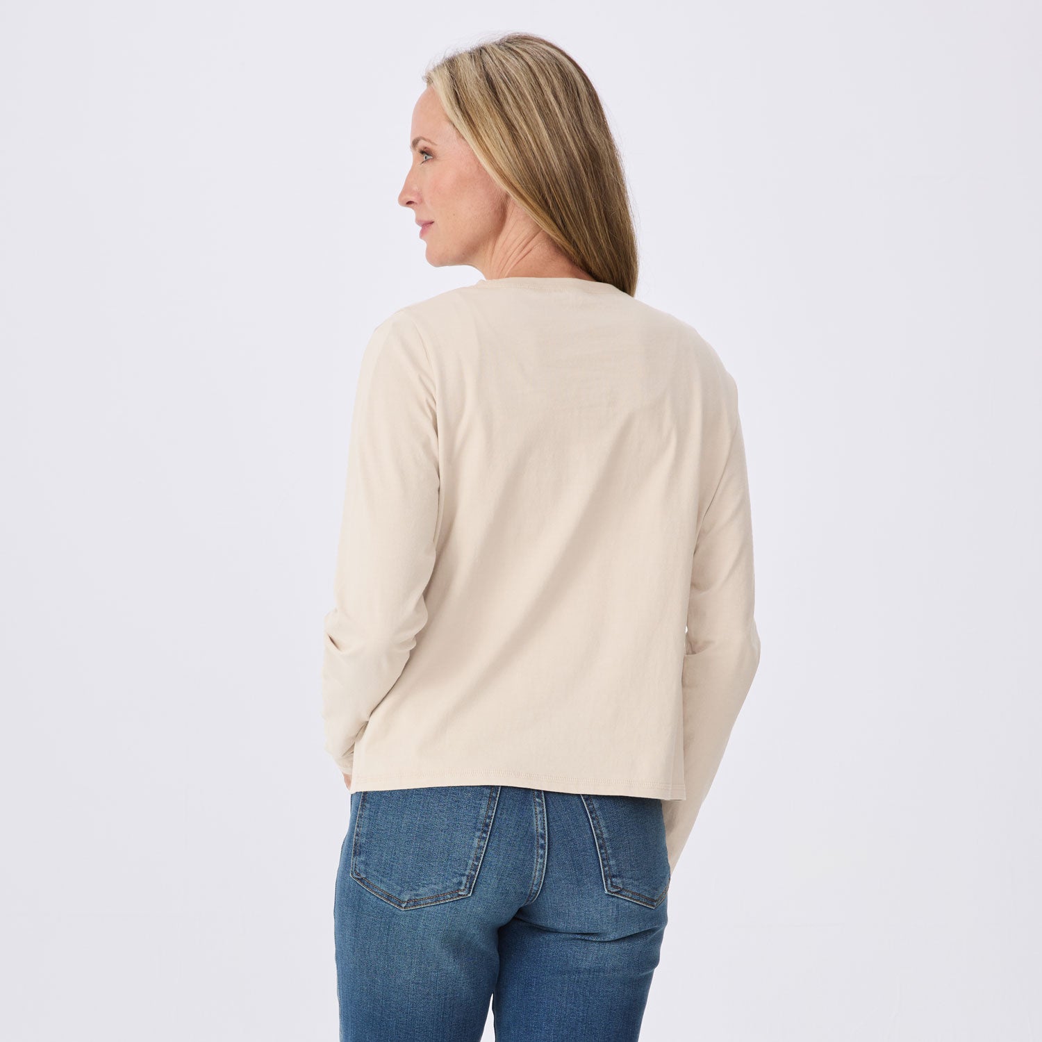 A woman shown from the back wearing a light beige long-sleeve top and blue jeans against a plain white studio background.